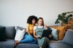 Tablet, Love And Lesbian Couple Relaxing On A Sofa In The Living Room Networking On Social Media. Rest, Digital Technology And Young Lgbtq Women Scroll On Mobile App Or The Internet Together At Home.